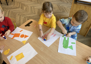dzieci przy stole przyklejają figury geometryczne n kartkę